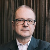 A person wearing glasses and a suit and tie Description generated with very high confidence